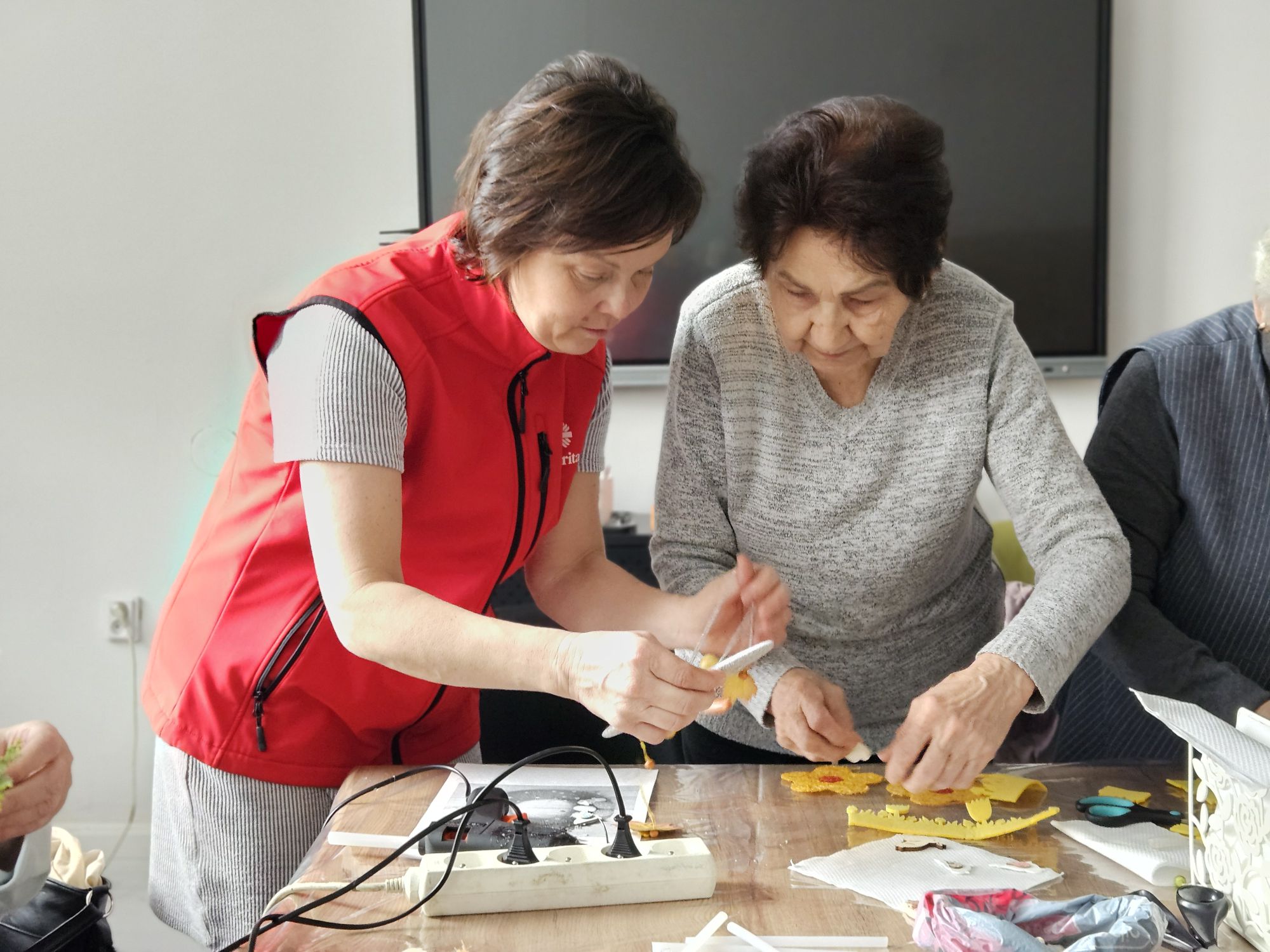 Dobrovoľníčka charity pomáha seniorke pri tvorivej dielni